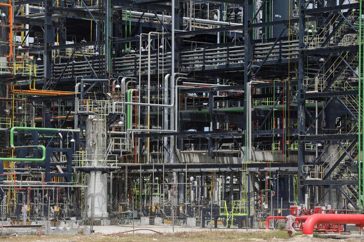 A large industrial refinery structure with elevated process equipment and heavy structural framing under construction.
